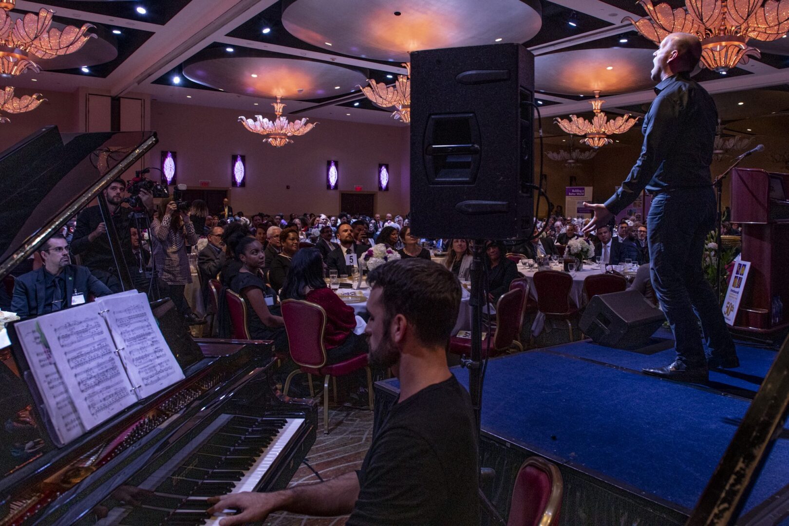 A man is playing a piano in front of a large group of people.